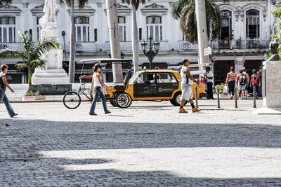 People and vehicles on road against buildings during sunny day