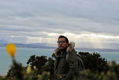 Portrait of young man standing at cloudy sky during sunset