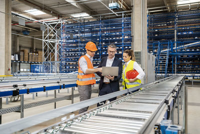 Blue-collar workers discussing over laptop with manager in warehouse