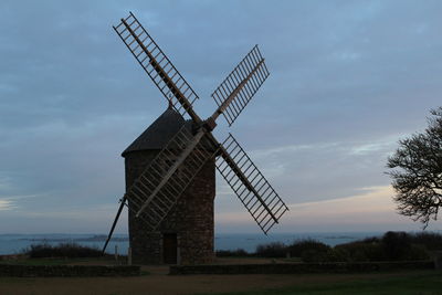 Traditional windmill on field against sky during sunset