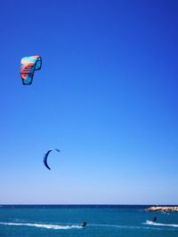 Person paragliding in sea against clear blue sky