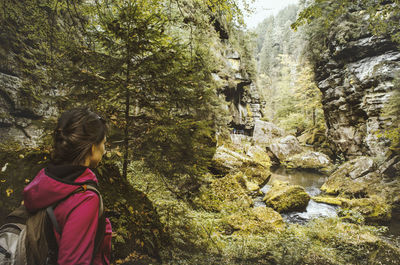 Rear view of woman standing amidst rocks in forest