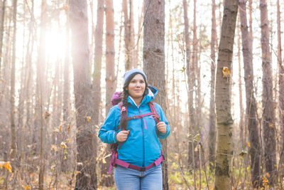 Smiling woman standing by tree trunk in forest