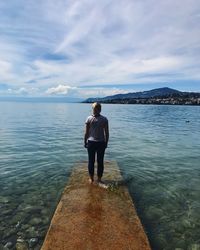 Rear view of woman standing on sea shore against sky