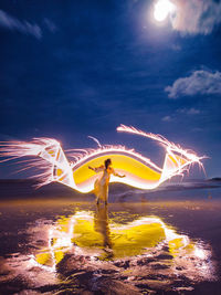 Person standing on illuminated street against sky at night