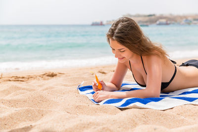 Smiling woman applying sunscreen while lying on towel at beach