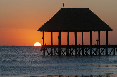 Silhouette built structure against sea during sunset