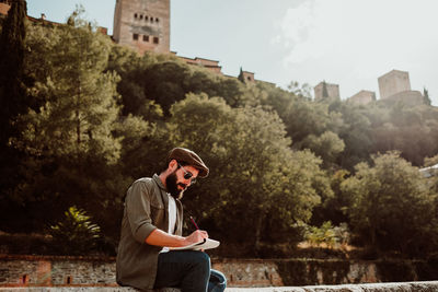 Man writing in book while sitting outdoors