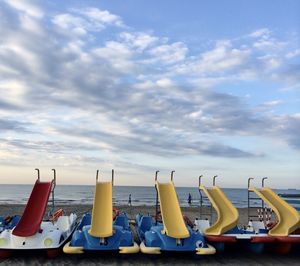Lounge chairs in row by sea against sky
