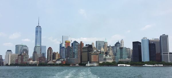 One world trade center amidst buildings in front of river against sky in city