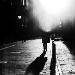 Silhouette of person walking on street amidst building