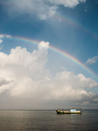 Boat sailing in sea against rainbow in sky