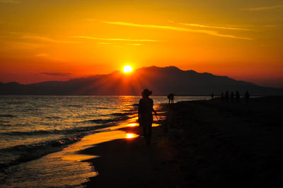 Silhouette man standing on beach against orange sky