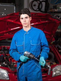 Portrait of mechanic with equipment standing against car in garage
