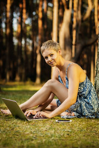 Portrait of woman using laptop while sitting in forest