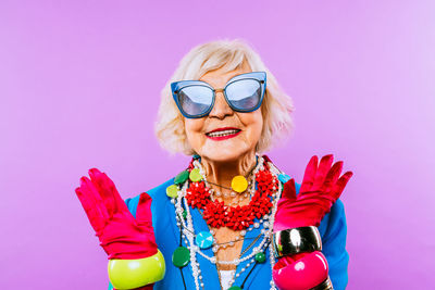 Portrait of smiling senior woman wearing sunglasses against pink background