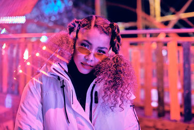 Portrait of smiling young woman standing in illuminated amusement park at night