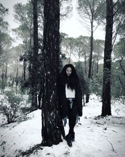 Full length portrait of woman leaning on tree in snow covered forest