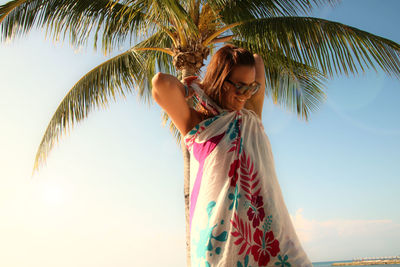 Woman wearing scarf while standing against palm tree