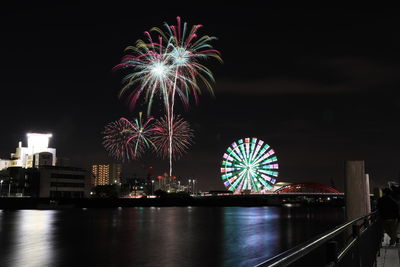 Firework display over illuminated city against sky at night