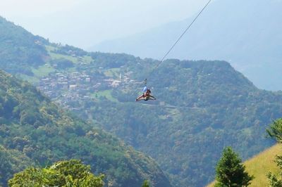 Low angle view of people on zip line against mountain and sky