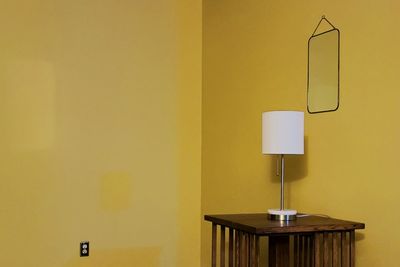Illuminated lamp on table against wall