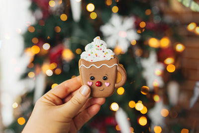 Hand holding christmas gingerbread cookie and decorations at christmas tree, gingerbread cup