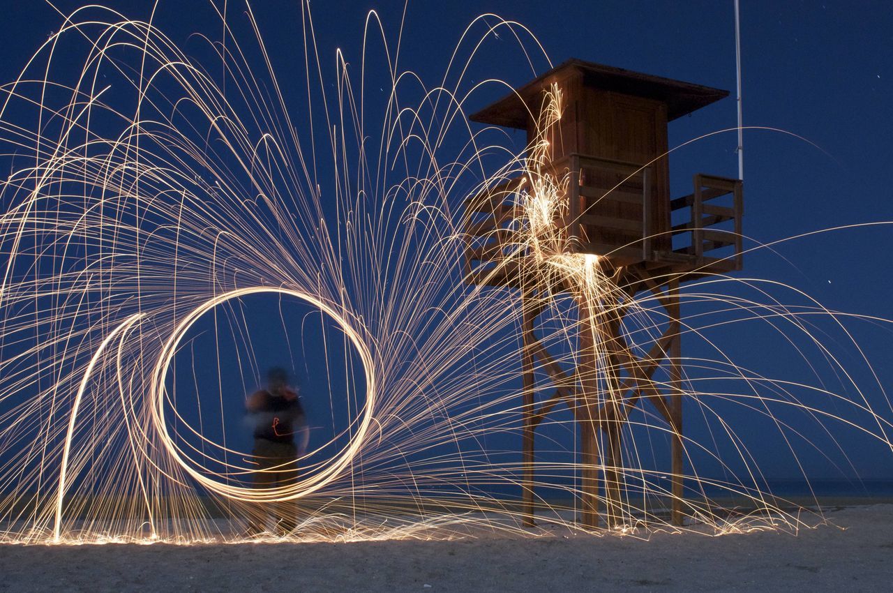 night, illuminated, long exposure, motion, light trail, arts culture and entertainment, blurred motion, speed, glowing, building exterior, street, city, sparks, spinning, lighting equipment, amusement park, outdoors, sky, built structure, street light