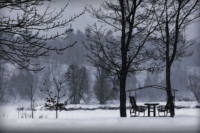 Silhouette trees on snow covered landscape against sky