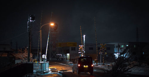 Illuminated street amidst buildings against sky at night