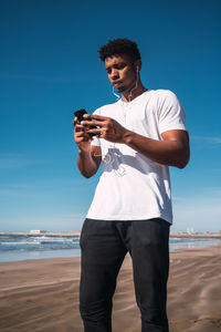 Young man using mobile phone at beach against sky