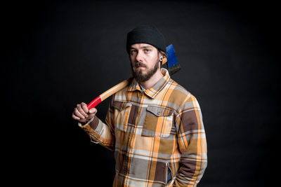 Portrait of lumberjack with axe over his shoulder against black background