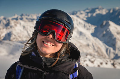 Beautiful girl in a black jacket, snow glasses and a helmet on her head, smiles in the winter