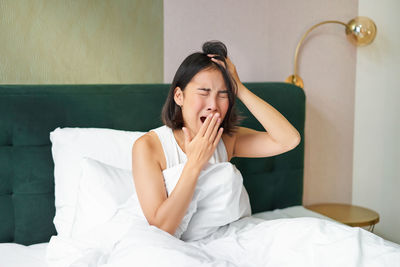 Young woman using mobile phone while lying on bed at home