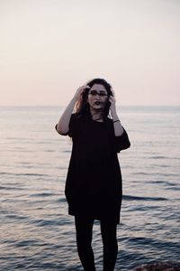 Woman standing on sea against sky during sunset