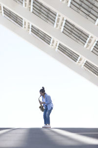 Woman with ponytail playing a saxophone while standing outdoors