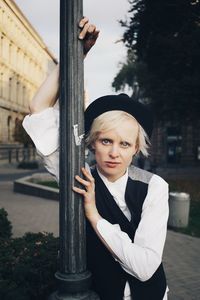 Portrait of young woman standing by pole against trees