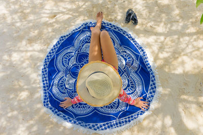 Directly above shot of woman wearing hat while sitting on beach towel