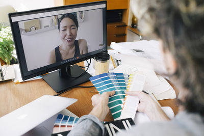 Smiling female architect discussing over color swatch on video call through computer