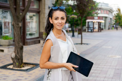 Confident young woman laughing and carrying notepad in hand while standing