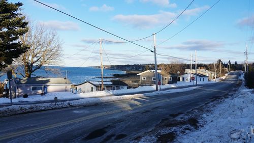 Road by houses and sea against sky during winter