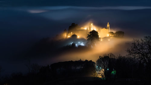 Silhouette trees and illuminated building against sky at night