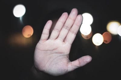 Cropped image of hand holding illuminated lights against black background