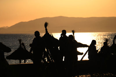 Silhouette people by sea against sky during sunset