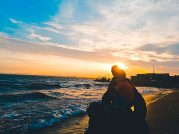 Rear view of silhouette woman standing at beach during sunset