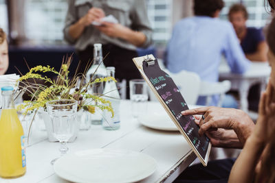 Cropped hand of woman holding menu while sitting with granddaughter in restaurant