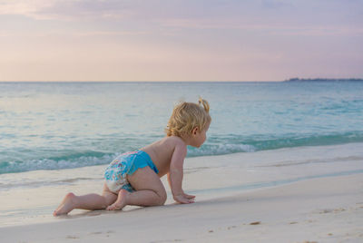 Full length of shirtless boy crawling at beach against sky