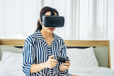 Young woman using vr goggles on bed