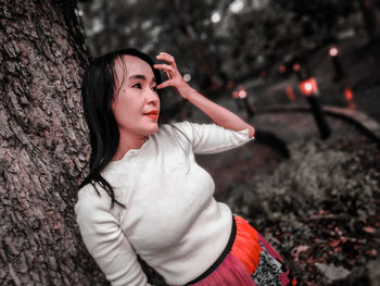 Young woman looking away while sitting on tree trunk