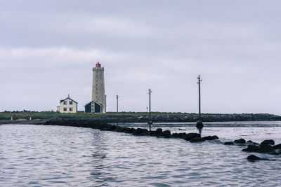 Lighthouse amidst sea and buildings against sky